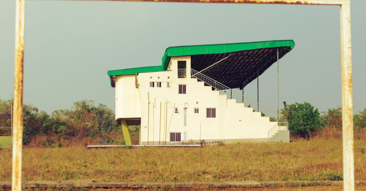 A building with green roof seen through rusty goalposts on a grassy sports field.