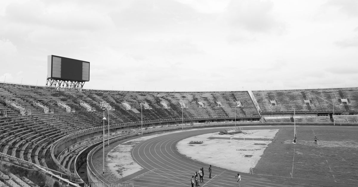 A vast black and white stadium with a few runners on the track. Captures emptiness and focus.