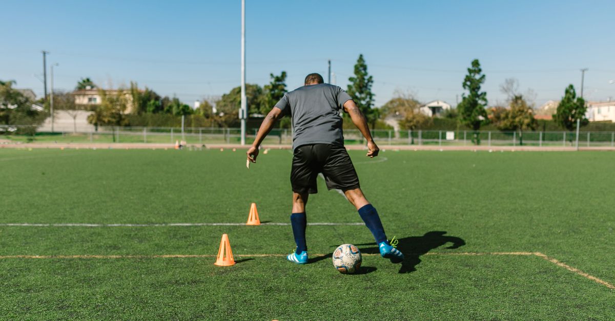 A soccer player practicing drills on a sunny day on an outdoor field.
